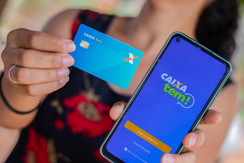 Mulher segurando celular com aplicativo caixa tem e cartão caixa tem mastercard.